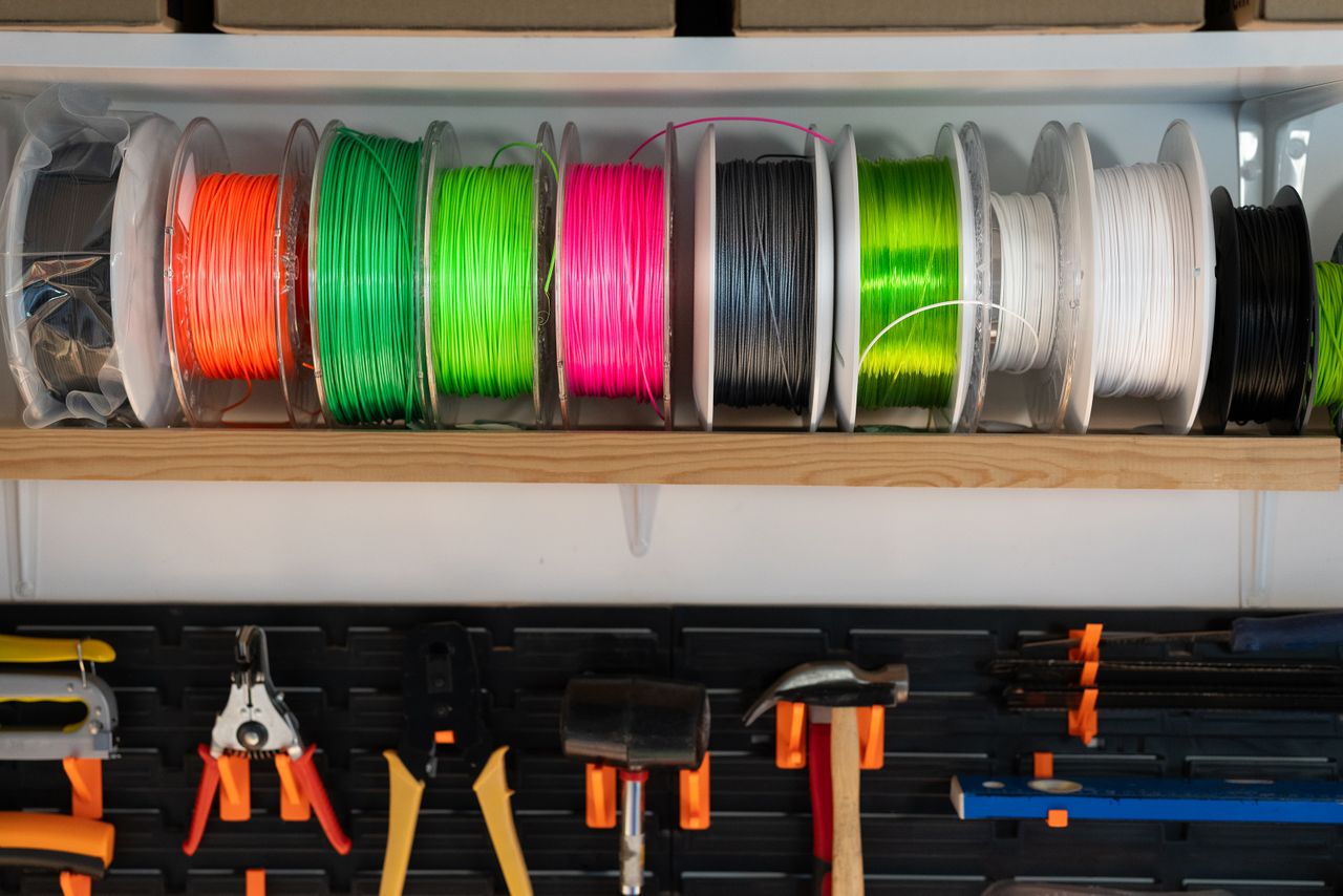 our-services-02 A variety of colorful filament spools and tools organized on a workshop shelf, ideal for 3D printing enthusiasts.