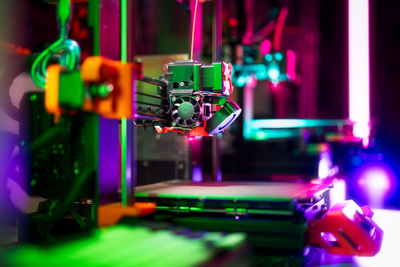 our-services-06 Close-up of a neon-colored 3D printer in a workshop, showcasing vibrant technology.