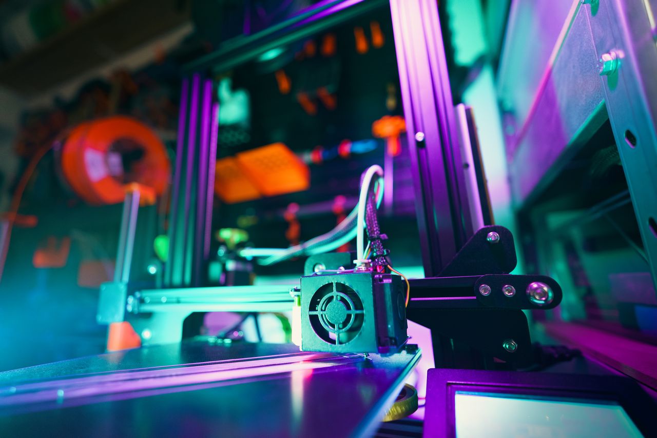 our-services-01 A close-up of a 3D printer in a neon-lit workshop, capturing technology and creativity.