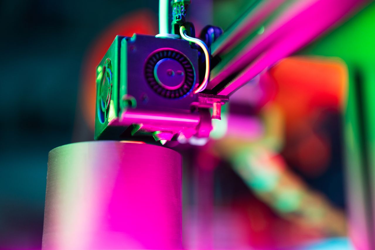 our-services-05 Close-up of a 3D printer in action under neon lighting, capturing vibrant colors and modern tech ambiance.