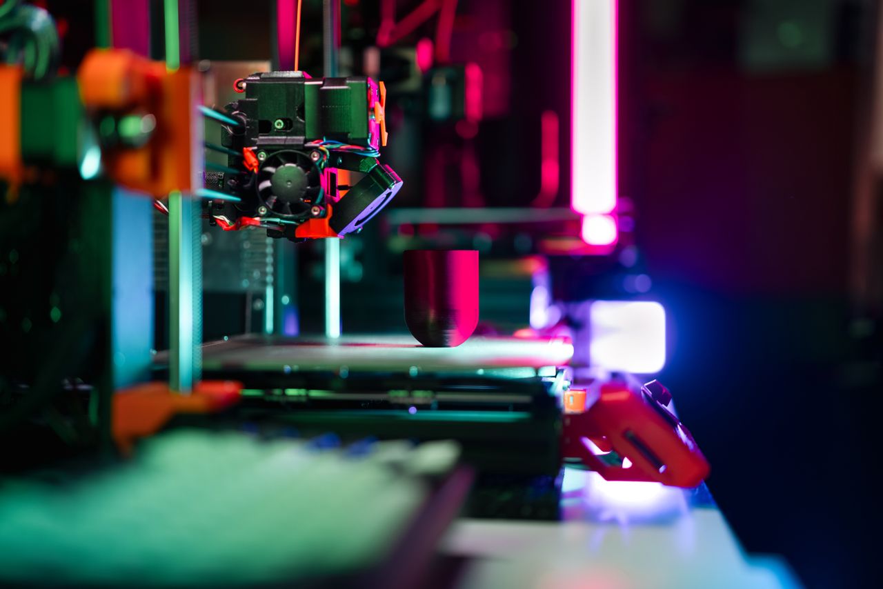 about-img Close-up of a modern 3D printer in a workshop, highlighted by neon lighting.